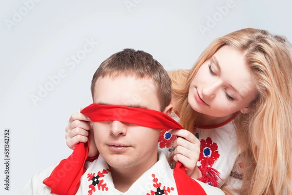 Fototapeta Two Loving Embraced Caucasian Couple in National Belarussian and Russian Decorated Costumes Playing With red Ribbon Against White Background.