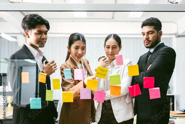 Fototapeta Group of successful Asian businessmen teamwork. Brainstorm meeting with sticky paper notes on the glass wall for new ideas. Using agile methodology for business in a tech start-up office.