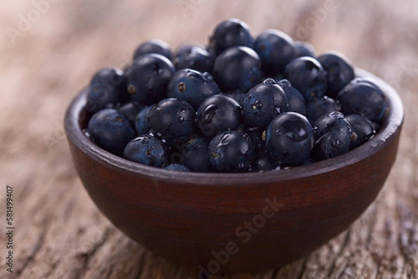 Fototapeta Fresh raw Patagonian Calafate berries (lat. Berberis heterophylla) in rustic bowl, photographed on wood (Selective Focus, Focus one third into the berries)