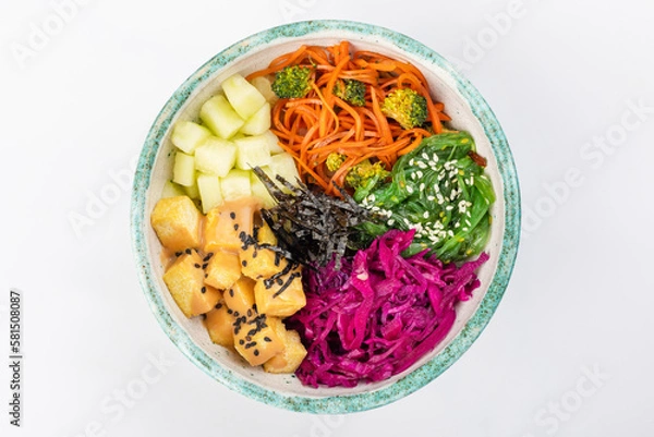 Fototapeta Bowl with tofu, carrots, broccoli, chuka, red cabbage, nori, white and black sesame seeds. Round green bowl on a white background. Top view.