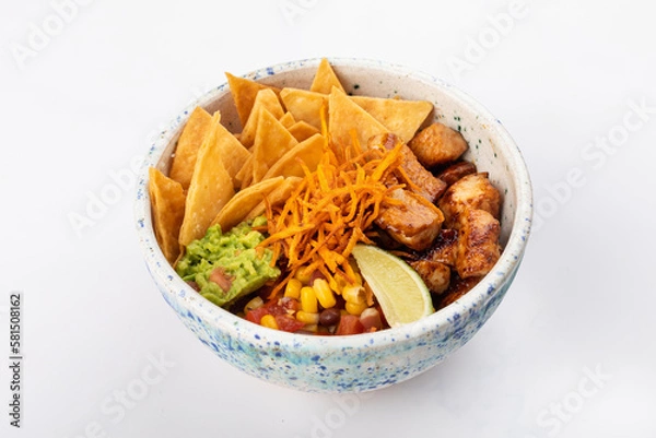Fototapeta Poke bowl with fried chicken, avocado, beans, corn, tomatoes, carrots, nachos, jalapenos and a lime wedge. Round bowl on a white background. Close up 3/4