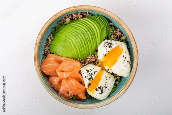 Fototapeta Poke bowl with quinoa, salmon, avocado and two poached eggs. Round blue ceramic bowl isolated on white background. Yolks spread Top view.