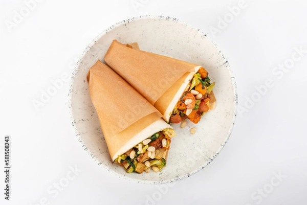 Fototapeta 2 vegetarian rolls with carrots, broccoli, tofu, tomatoes, zucchini, pine nuts on a round white plate on a white background. Top view.
