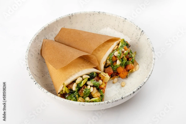 Fototapeta 2 vegetarian rolls with carrots, broccoli, tofu, tomatoes, zucchini, pine nuts and pesto sauce on a round white plate on a white background. Close up 3/4