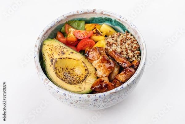 Fototapeta Poke bowl with quinoa, grilled avocado half, roasted pineapples, cherry tomatoes, lettuce and fried chicken in dark sauce. Light green ceramic plate on a white background. Close up 3/4