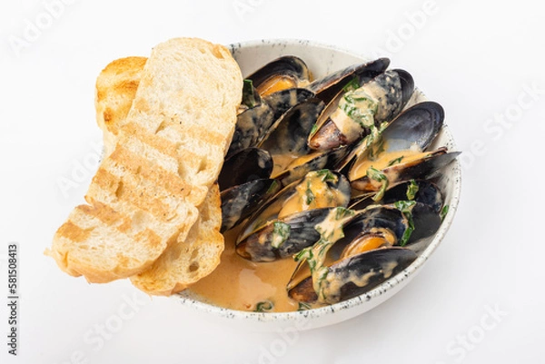 Fototapeta A dish of mussels with herbs in a sauce on a light round ceramic plate with two toasted toasts. White background, close up 3/4