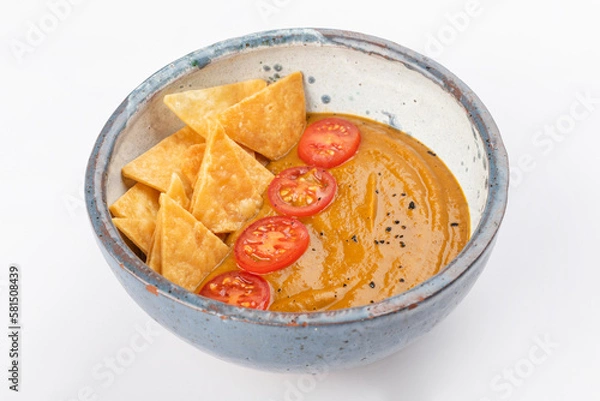 Fototapeta Pumpkin cream soup with cherry tomatoes and nachos. Round gray ceramic bowl isolated on white background. Close up
