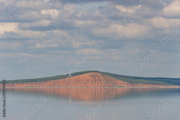 Fototapeta lake with clouds in the sky, red hill with forests on background. hill symmetric reflection in the water.A waterfowl with a tufted crest on its head