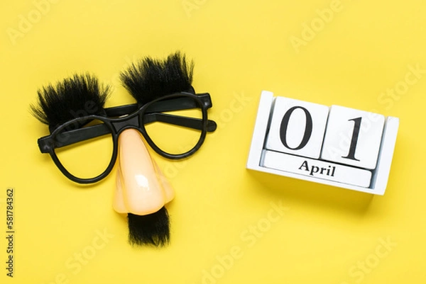 Fototapeta funny face - fake eyeglasses, nose and mustache, calendar with date 01 April on yellow background Happy fools day concept 1st April party Holiday greetind card