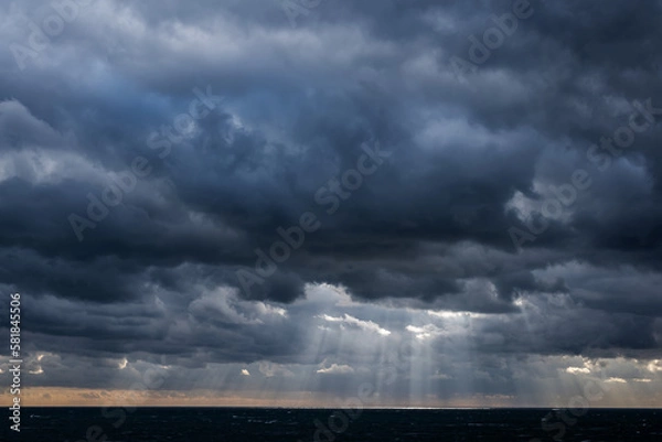 Obraz Distant sun rays through dark storm clouds over a dark sea