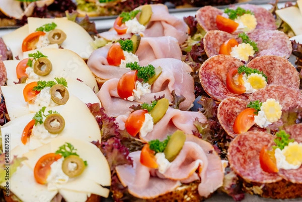 Obraz Belegte Brote mit Schinken, Käse und Salami, dekoriert mit Salat, Butter, Tomate, Gewürzgurke und Olive auf Häppchen Platte bei einer Party wie Geburtstagsfeier oder Hochzeitsfeier als Snack