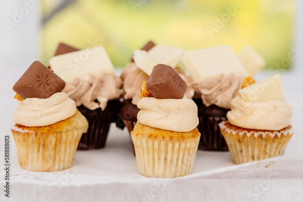 Obraz Cupcakes und Muffins mit Vanillecreme Topping und Schokoladenstück als Deko im Kuchenbuffet
