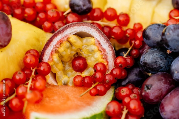 Obraz saftiger und gesunder Gelber Granatapfel aufgeschnitten und mit Johannisbeeren dekoriert und Weintrauben im Hintergrund auf Obstplatte bei Gartenparty oder Geburtstagsfeier