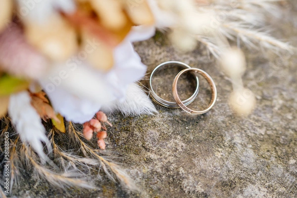 Obraz Eheringe in Rose, Gold und Silber auf Stein mit Brautstrauß im Vordergrund
