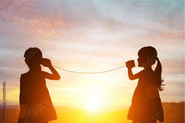 Obraz Silhouette of Two female kids stands and talking by using string can phone on beautiful sunset sky