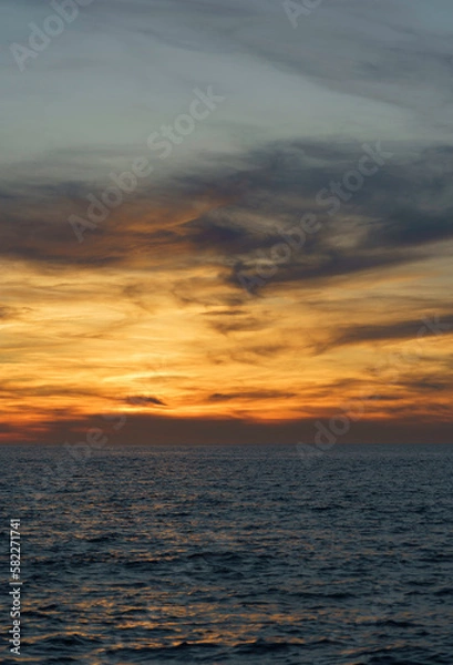 Obraz This beautiful photograph was taken at sunset on the beach, showcasing a stunning view of an island in the background. The sky has a warm orange hue, creating a serene and peaceful ambiance as the sun