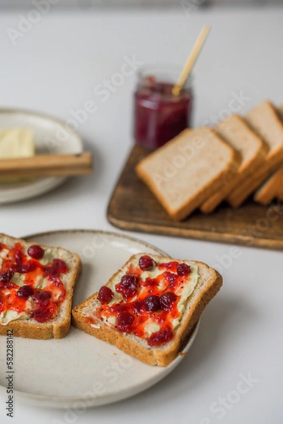 Obraz Bread with butter and cranberry jam is on the table and ready to eat. A delicious and sweet breakfast. Aesthetically pleasing serving of food. Recipe for toast with butter and jam.