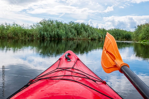 Fototapeta Kayaker point of view. Red kayak bow with a view on the river and rushes.   River kayaking concept. Active vacations in wild nature.
