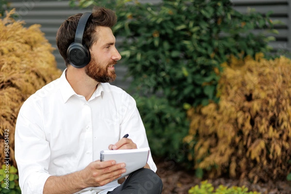 Fototapeta Man listening music in headphones while writing in diary