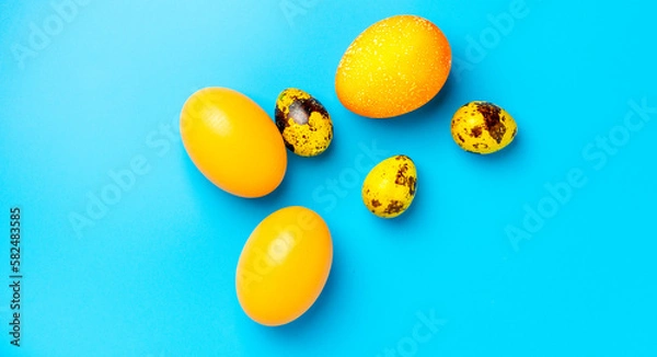 Fototapeta Easter background with yellow Easter eggs and spring flowers on a blue background. Top view, space for text, banner