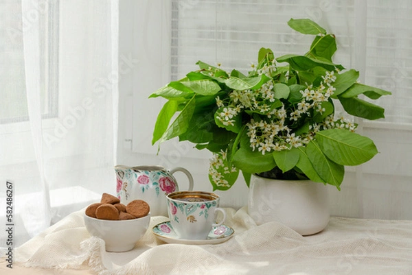 Fototapeta still life, bouquet spring bouquet of fragrant bird cherry, tea with sweets, a book on the windowsill by the window and tea on the windowsill, tea drinking on vacation in the summer.