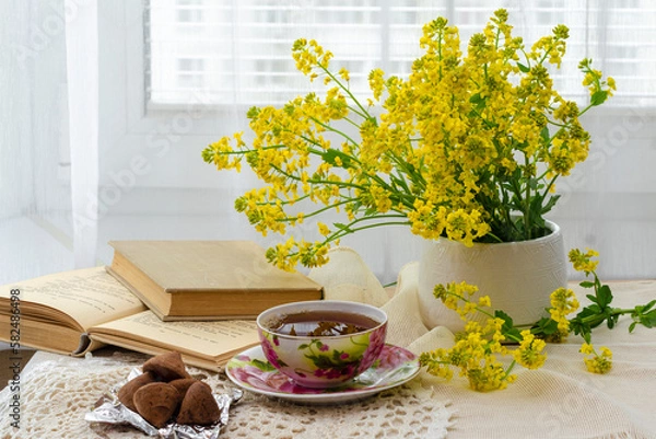 Fototapeta still life, bouquet of yellow wild flowers, tea with sweets, a book on the windowsill near the window and tea on the windowsill, tea party on vacation in summer