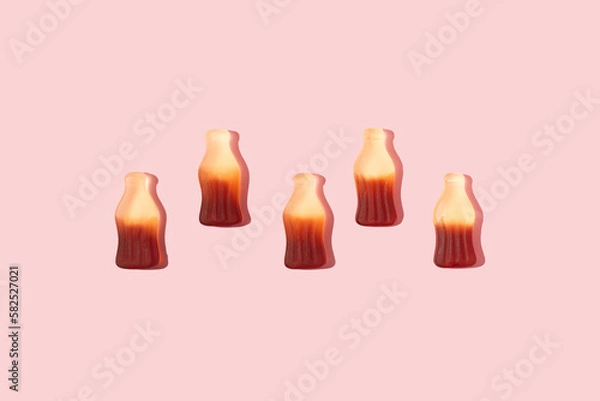 Obraz Bottle shaped gummy candies with sunlight shadows assorted in a line on pink background.