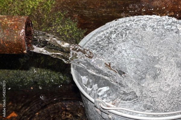 Fototapeta Pailful of water filling from the tube of spring closeup