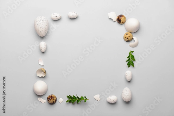 Fototapeta Frame made of Easter eggs and plant leaves on grey background