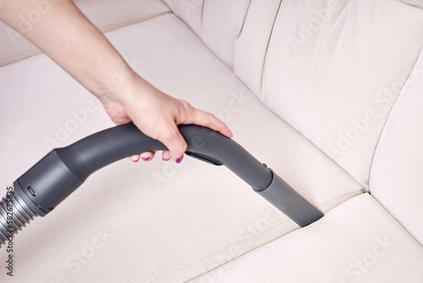 Obraz Close-up of a female hand vacuums the surface of the beige sofa