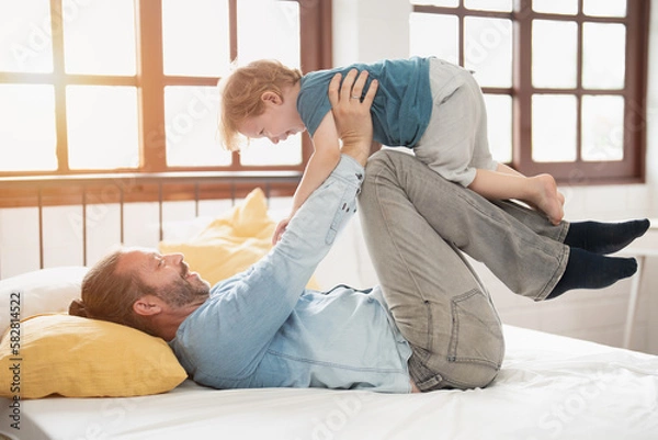 Fototapeta Happy father lying and lift up son or daughter in airplane gesture, playing and spend family quality time,   happy family, with love and care, parent and child, father bond.