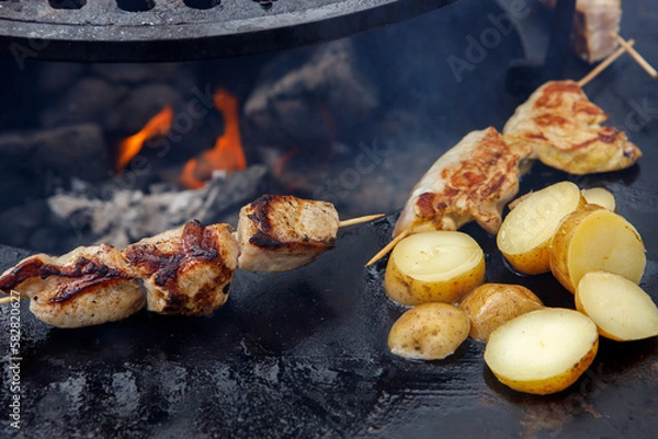 Fototapeta Potatoes in the peel and pieces of chicken meat, grilled, lie on the grill.