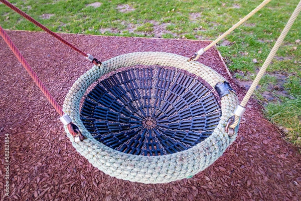 Fototapeta Close up of birds nest children's play swing hanging from rope in outdoor playground with soft floor