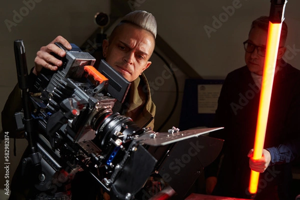 Fototapeta two handsome caucasian men are filming a movie on a film set with a professional movie camera with extra light astera in hand
