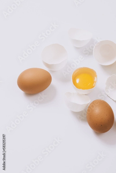 Obraz Whole brown eggs and cracked white eggs half with a yolk on bright background. Selective focus.
