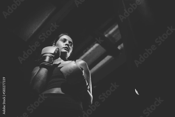 Fototapeta Dark Haired Girl Boxing a Punching Bag in a Moody Setting