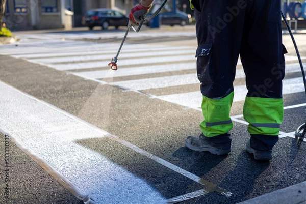 Fototapeta Process of making new road surface markings with a line striping machine, workers improve city infrastructure, demarcation marking of pedestrian crossing with a hot melted paint on asphalt pavement