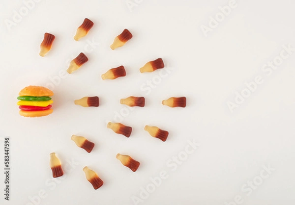 Fototapeta Gummy candies in burger and bottles shape arranged in line on white background. Food compatibility concept.