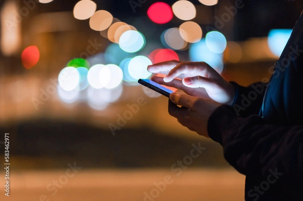 Fototapeta Close-up shot of an unrecognizable man using a phone in the city at night.