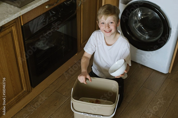 Fototapeta Boy In Kitchen Making Compost Scraping Vegetable Leftovers Into Bin