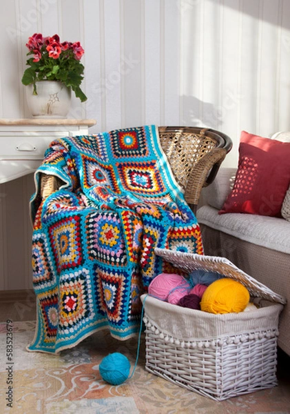 Obraz Bright beautiful hand-knitted plaid on a wicker chair and a basket with colored yarn