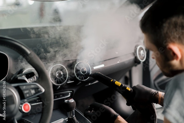 Fototapeta The concept of car cleaning and detailing The detailing master cleans the car interior with a hot steam cleaner Cleaning the car interior