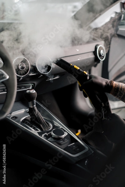 Fototapeta The concept of car cleaning and detailing The detailing master cleans the car interior with a hot steam cleaner Cleaning the car interior