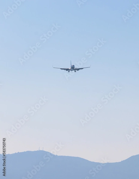 Fototapeta View of modern passenger plane aircraft in flight, commercial airplane flying in the sky before take off or landing, with mountains in the background in a summer sunny day