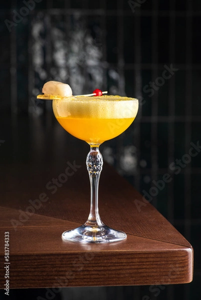 Fototapeta Yellow alcoholic cocktail with white foam. Cocktail glass. Wooden table on background