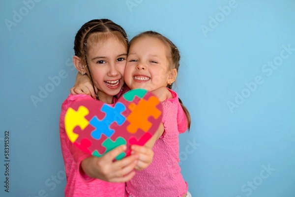 Obraz Funny laughable girls show a heart- shaped postcard with pieces of multicolored puzzles . Heart in Viva Magenta color for children with autism