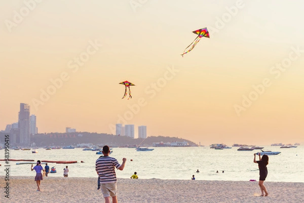 Fototapeta People relaxing on sea coast, girl talking on phone, dad and daughter flying kite, selective focus.