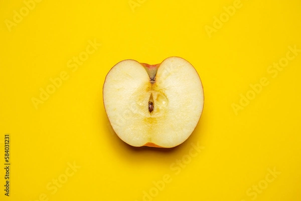 Fototapeta A juicy organic red apple cut in half on a yellow background. Cool minimal flat lay, copy space