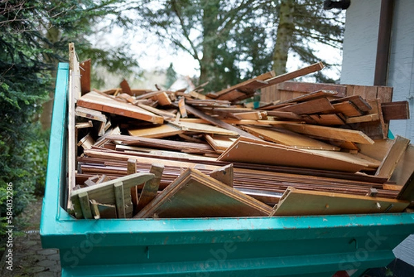 Obraz green recycling container filled with wood, next to a house