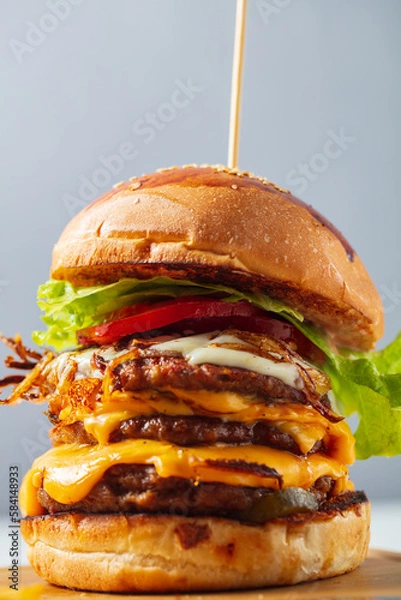 Fototapeta Loaded cheeseburgers three triple, stacked patties stacked high with layers of cheese, lettuce, and tomato. Tall cheeseburger. High quality photo